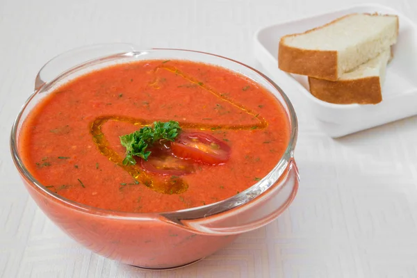 Délicieuse soupe rouge aux herbes dans une assiette transparente, et pain sur une nappe blanche. Cadre horizontal — Photo