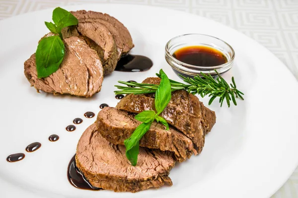 Delicious, mouth-watering pieces of roasted meat with herbs and sauce, on a white plate. Horizontal frame