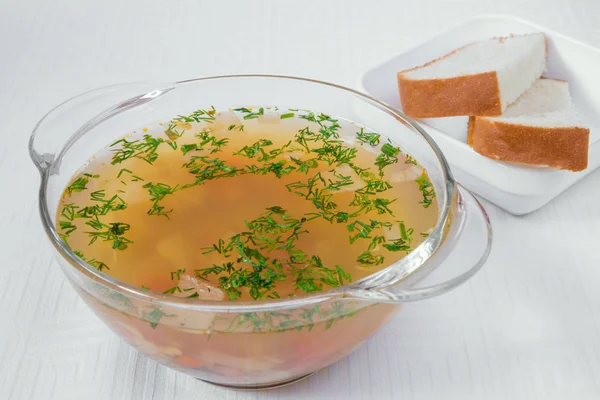 Lezzetli, lezzetli hafif kahverengi çorbası ile şeffaf bir tabak içinde otlar. Beyaz bir tabak içinde ekmek. Yatay Çerçeve — Stok fotoğraf