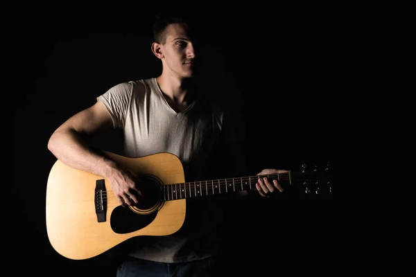 Guitarist, music. A young man plays an acoustic guitar on a black isolated background. Horizontal frame — Stock Photo, Image