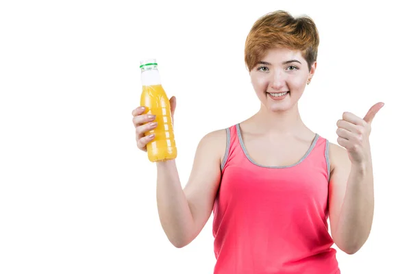 Здоровый образ жизни, здоровое питание. Молодая девушка с бутылкой апельсинового сока в руке, улыбаясь с большим пальцем вверх, на белом изолированном фоне. Горизонтальная рамка — стоковое фото