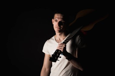 Müzik ve yaratıcılık. Bir T-shirt ve jeans yakışıklı genç adam bir akustik gitar ile onun omzuna izole siyah bir arka plan üzerinde duruyor. Dikey Çerçeve