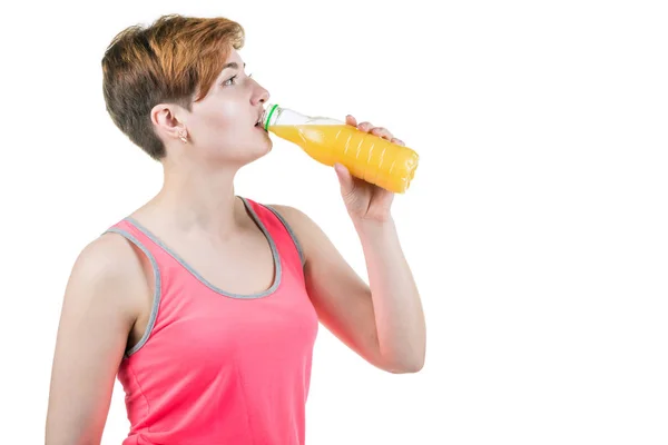 Здоровый образ жизни, здоровое питание. Молодая девушка пьет апельсиновый сок из бутылки, изолированной на белом фоне. Горизонтальная рамка — стоковое фото