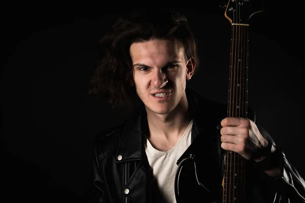 Music and creativity. Handsome young man in a T-shirt, jacket and jeans, with an electric guitar, on a black isolated background. Horizontal frame — Stock Photo, Image