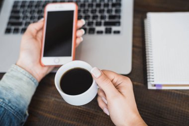 Üstten Görünüm tablosunun içen sabahları kahve masada bir fincan kahve, bir dizüstü bilgisayar ve cep telefonu ile ağ onu laptop sörf bir genç kızın üstünde. Yatay Çerçeve