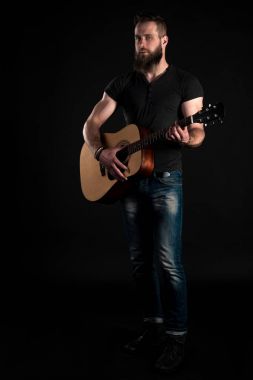 Bir sakallı bir karizmatik ve şık adam tam uzunlukta standları ve akustik gitar, siyah bir izole arka planda çalar. Dikey Çerçeve