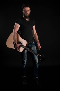 Karizmatik ve şık bir adam sakallı bir akustik gitar izole siyah bir arka plan ile tam uzunlukta duruyor. Dikey Çerçeve