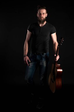Karizmatik ve şık bir adam sakallı bir akustik gitar izole siyah bir arka plan ile tam uzunlukta duruyor. Dikey Çerçeve
