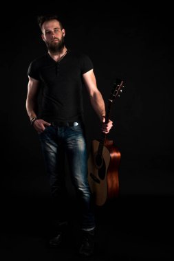 Karizmatik ve şık bir adam sakallı bir akustik gitar izole siyah bir arka plan ile tam uzunlukta duruyor. Dikey Çerçeve