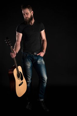 Karizmatik ve şık bir adam sakallı bir akustik gitar izole siyah bir arka plan ile tam uzunlukta duruyor. Dikey Çerçeve