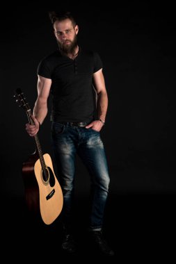 Karizmatik ve şık bir adam sakallı bir akustik gitar izole siyah bir arka plan ile tam uzunlukta duruyor. Dikey Çerçeve