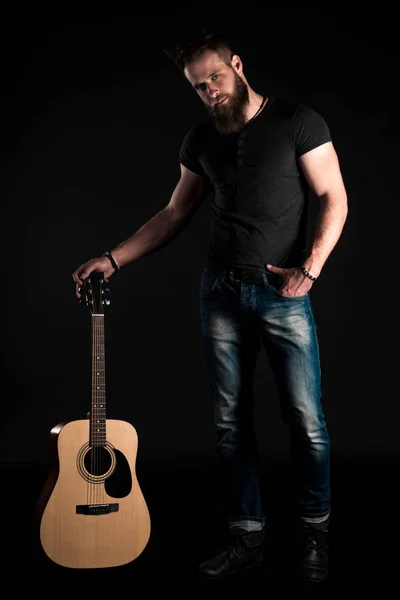 Egy akusztikus gitár, fekete elszigetelt alapon egy karizmatikus és elegáns férfi szakáll áll teljes hosszúságú. Függőleges keret — Stock Fotó