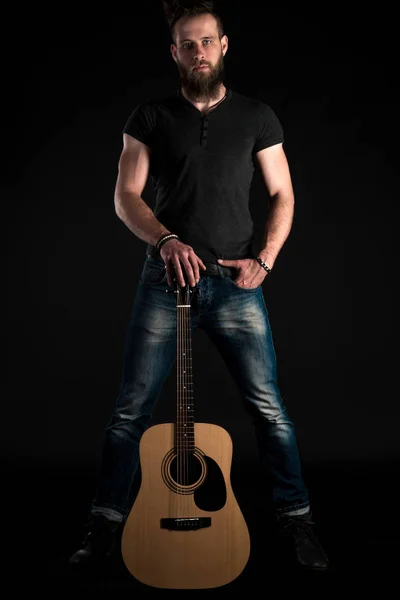 Egy akusztikus gitár, fekete elszigetelt alapon egy karizmatikus és elegáns férfi szakáll áll teljes hosszúságú. Függőleges keret — Stock Fotó
