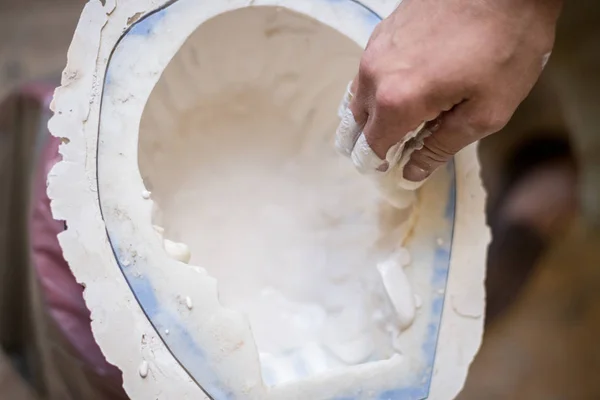 The sculptor's hands fill the white liquid into the mold. Horizontal frame