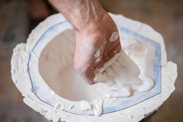 The sculptor\'s hands fill the white liquid into the mold. Horizontal frame