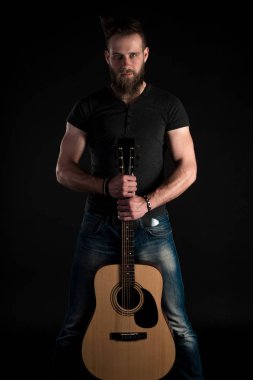 Karizmatik ve şık bir adam sakallı bir akustik gitar izole siyah bir arka plan ile tam uzunlukta duruyor.