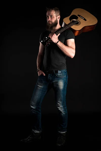 A karizmatikus és elegáns férfi szakáll áll teljes hosszúságú elszigetelt fekete alapon akusztikus gitár. — Stock Fotó