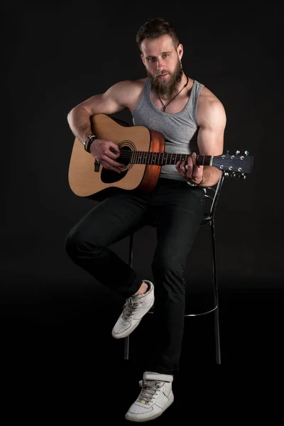 Харизматичний чоловік з бородою, грає на акустичній гітарі, на чорному ізольованому тлі. Вертикальна рамка — стокове фото