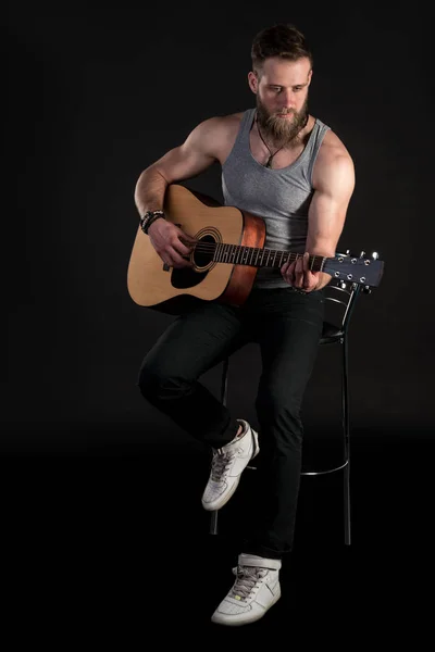 Ένας χαρισματικός άνθρωπος με μια γενειάδα, παίζει μια ακουστική κιθάρα, σε ένα μαύρο απομονωμένες φόντο. Κατακόρυφο πλαίσιο — Φωτογραφία Αρχείου