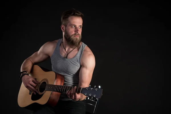 Харизматичний чоловік з бородою, грає на акустичній гітарі, на чорному ізольованому тлі. Горизонтальна рамка — стокове фото