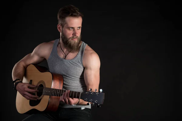 Um homem carismático com uma barba, tocando uma guitarra acústica, em um fundo preto isolado. Quadro horizontal — Fotografia de Stock