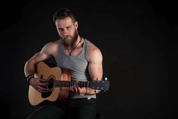 Um homem carismático com uma barba, tocando uma guitarra acústica, em um fundo preto isolado. Quadro horizontal — Fotografia de Stock