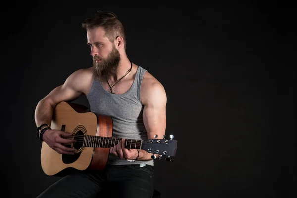 Um homem carismático com uma barba, tocando uma guitarra acústica, em um fundo preto isolado. Quadro horizontal — Fotografia de Stock