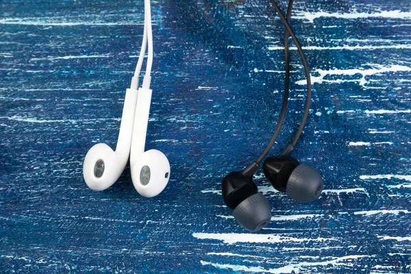 Pequenos fones de ouvido brancos e pretos estão em um fundo azul denim. Quadro horizontal — Fotografia de Stock