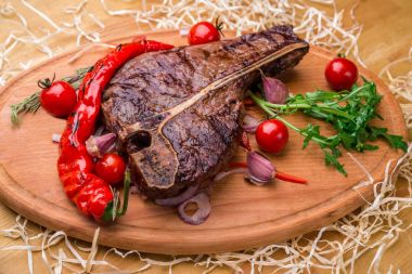 İştah açıcı biftek bir kemik, domates, biber, bir ahşap tahta üzerinde. Yatay Çerçeve