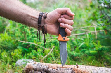 Avcılık, zor koşullarda hayatta kalma. Bir adamın elini bir av bıçağı aðaca ekler. Yatay Çerçeve