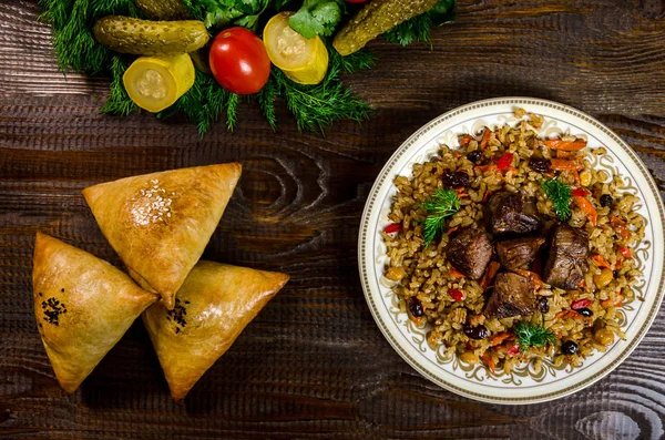 Plato nacional uzbeko de pilaf y samsa sobre un fondo de madera oscura — Foto de Stock