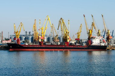 Arka planda sarı vagonlar ve kapsayıcılar limanda büyük gemi