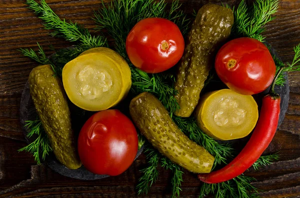 Nakládaná zelenina: okurky rajčata, cuketa a byliny roztroušených na dřevěné pozadí — Stock fotografie