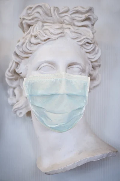 Sculpture of the face of a beautiful Greek woman in a medical mask. Quarantine during coronavirus. Vertical frame