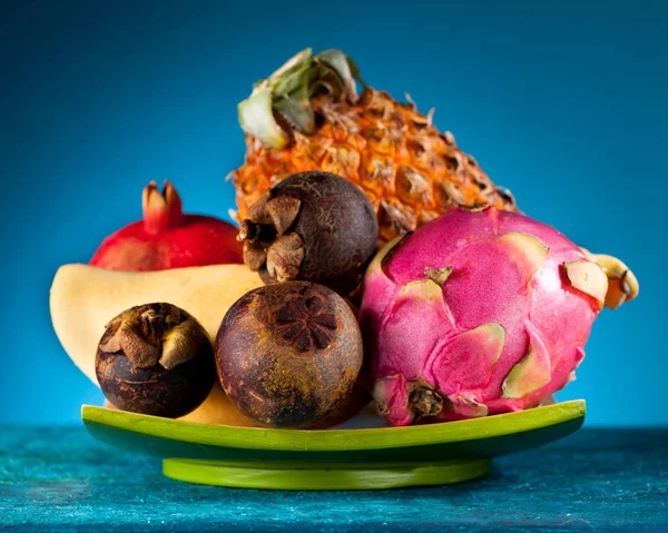 Exotic fruit: dragon, pineapple, mangosteen, mango and pomegranate on a blue background