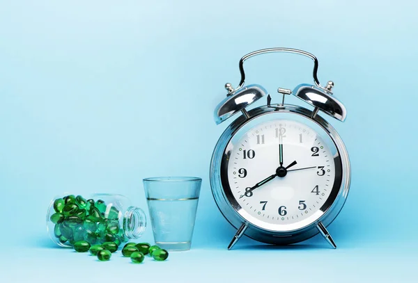 Medical pills, glass water and metal alarm clock on a blue background, concept medicine and treatment