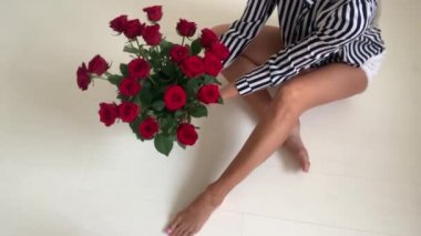Güzel uzun bacaklı bir kadın yere oturur ve bir buket gül düzeltir.