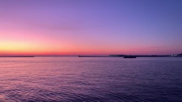 夕日の湾の景色は 空が美しい色で描かれており 波が海に沿って行き ボートが浮かぶ — ストック動画