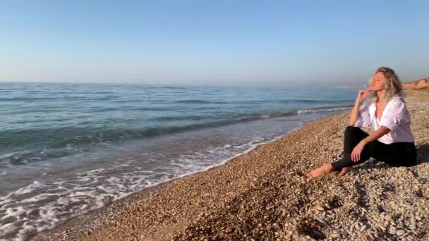 Vacker Blond Kvinna Sitter Och Mediterar Stranden Nära Vågorna Blå — Stockvideo