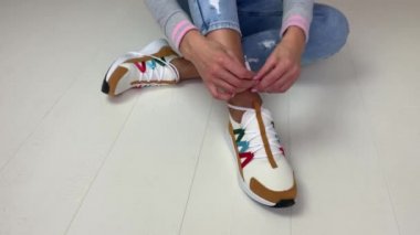 Beyaz spor ayakkabılı atletik bir kadın yerde oturmuş ayakkabı bağcıklarını bağlıyor..