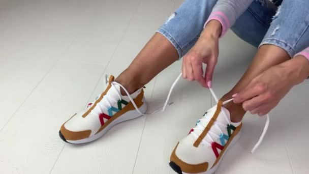 Atletisk Kvinna Fashionabla Vita Sneakers Jeans Sitter Golvet Och Knyta — Stockvideo