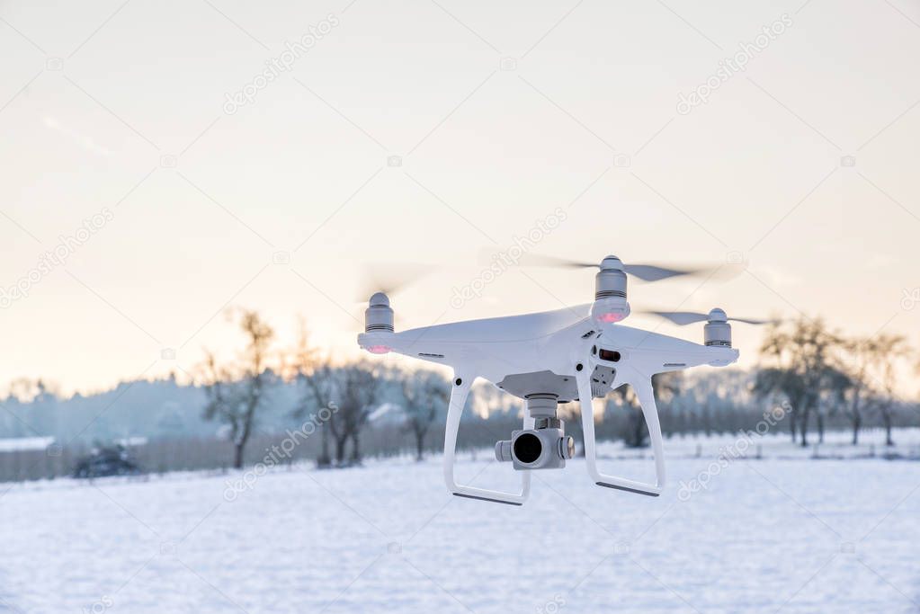 White drone camera floating in air with white snow and field in 