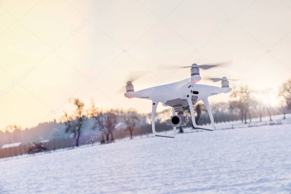 White drone camera floating in air with white snow and field in 