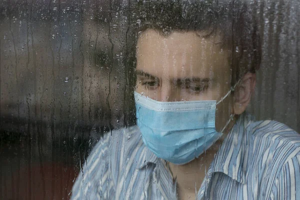 Yüz maskesi takan genç bir adam, COVID-19 hastası ve karantinaya alınmış, hastane penceresinden dışarı bakıyor.