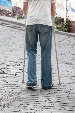 Engelli kişi parkta koltuk değneği üzerinde yürüyor.