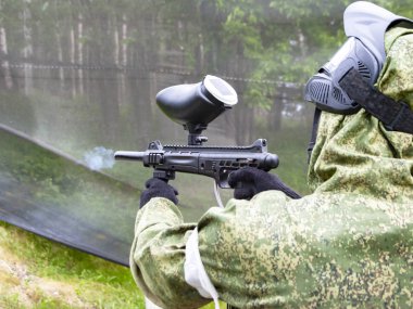 Paintball oynayan bir adam yaz günü antrenman sahasında makineli tüfek ateşler.