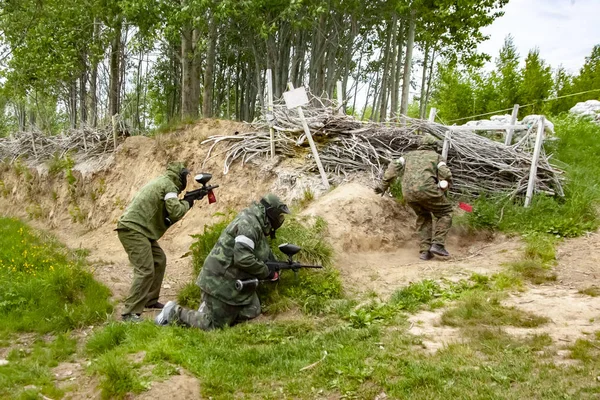 Tres personas jugando paintball se escondieron detrás de una valla de mimbre en un día brillante — Foto de Stock