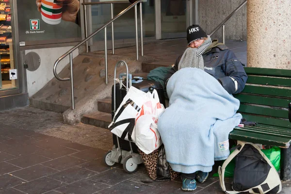 Bezdomovec se všemi věcmi spí na lavičce u obchodu — Stock fotografie