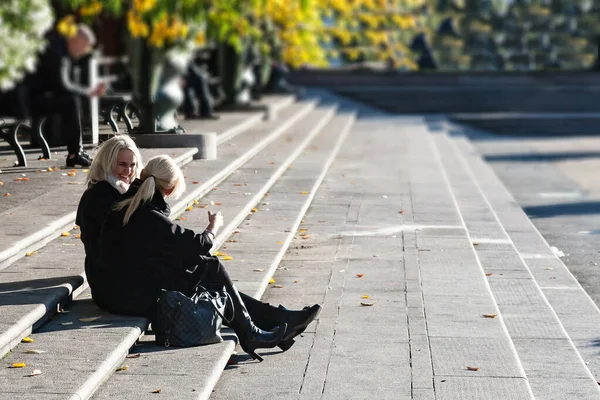 İki güzel kız hareketli bir şekilde konuşuyor, Stockholm parkının merdivenlerinde oturuyorlar. — Stok fotoğraf