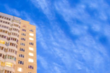 Bulanık bir arka plan, yanan pencereleri ve bulutlu güzel bir akşam gökyüzünün arka planına sahip bir apartman gibi.